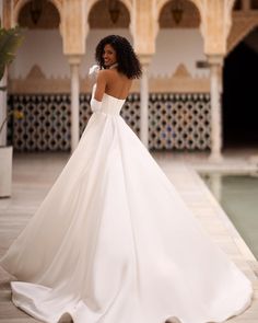 a woman in a white wedding dress is standing near a pool and looking off into the distance