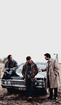 three men are standing next to a car