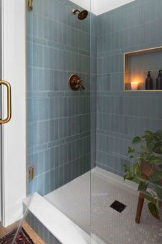 a bathroom with blue tile and gold fixtures, including a glass shower door that opens up to the bathtub