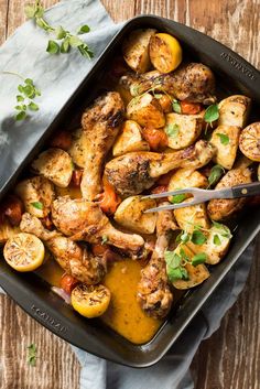 a pan filled with chicken and vegetables on top of a wooden table