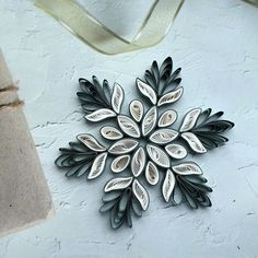 a metal snowflake hanging on a white wall next to a brown bag and ribbon