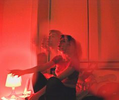 two people sitting on a bed in a room with red light