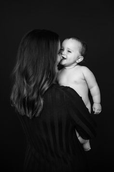 a woman holding a baby in her arms and kissing it's face with the other hand