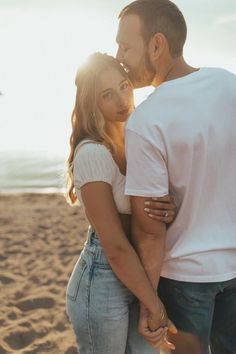 a man and woman standing next to each other on the beach with their arms around each other