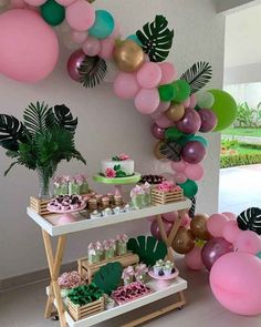 a table topped with lots of pink, green and gold balloons next to a wall