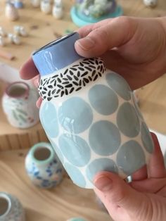 a person is holding a blue and white coffee mug in front of many other cups