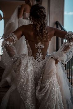 the back of a woman's wedding dress as she stands on stairs in front of other brides