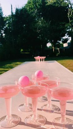 four glasses filled with pink liquid sitting on top of a cement slab next to trees