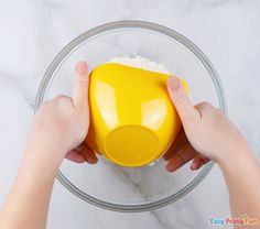 someone is mixing ingredients in a bowl with their hands on the bottom and one hand holding an orange measuring cup