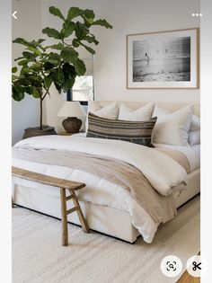 a bed with white sheets and pillows next to a potted plant in a bedroom