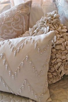 two decorative pillows on a bed with white linens and beaded trim around the edges