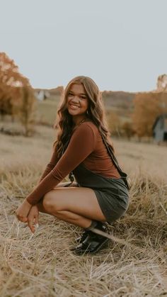 a woman kneeling down in a field with her legs crossed and smiling at the camera