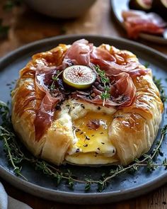 a pastry topped with ham and cheese on top of a blue plate next to sliced figs