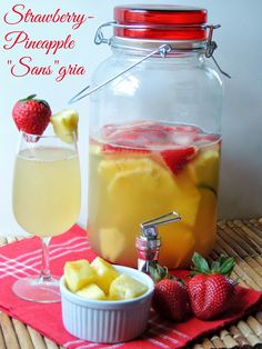 a pitcher of pineapple sangria next to a bowl of strawberries and a glass of wine