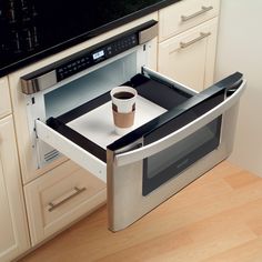 a coffee cup is sitting in the middle of an open microwave drawer that's on top of a counter