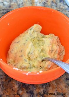 an orange bowl filled with food sitting on top of a counter next to a spoon