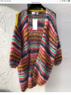 a multicolored sweater hanging on a white wall with a tag attached to it