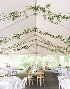 an outdoor tent with tables and chairs covered in greenery