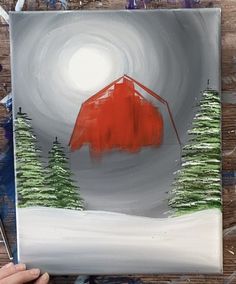 someone is painting a red barn in the snow with pine trees on it's side