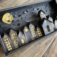 a wooden box with houses and bats in it on a wood table next to a candle