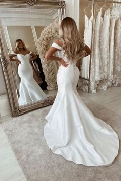 a woman standing in front of a mirror wearing a white dress and looking at her reflection