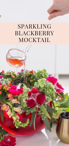 someone is pouring wine into a red bowl filled with flowers and greenery on the table