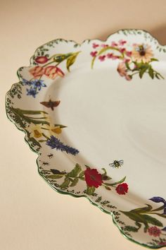 a white plate with colorful flowers on the rim and green trim around the edge is sitting on a table