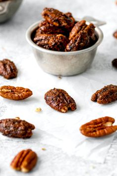 pecans and other nuts are scattered around a small metal bowl on a white surface