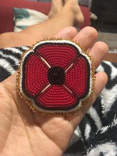 a hand holding a red and black beaded brooch in it's palm