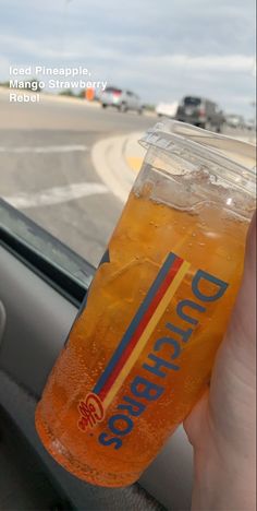 a person holding up a drink in front of a car window with the word bud on it