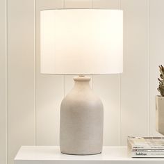 a white lamp sitting on top of a table next to a book and potted plant