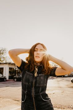 a woman in overalls is standing on the street with her hands behind her head