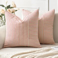 two red and white striped pillows sitting on a couch next to a vase with flowers