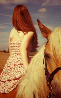 a woman in a dress riding on the back of a brown and white horse next to a field