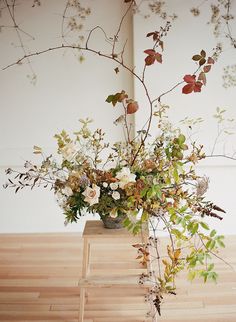 a vase filled with lots of flowers on top of a wooden table next to a wall