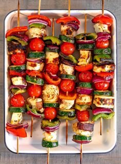 grilled vegetables on skewers with tomatoes and peppers in a white dish over a wooden table