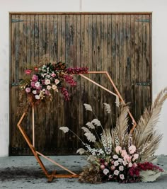 an arrangement of flowers and plants in front of a wooden wall with a geometric frame