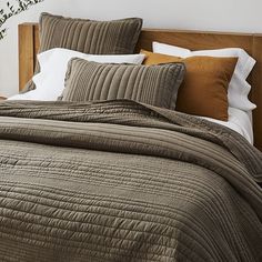 a bed with brown comforter and pillows on top of it, next to a plant