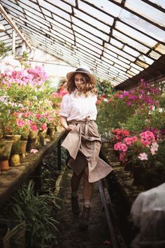 a woman in a hat is walking through a greenhouse filled with pink and white flowers