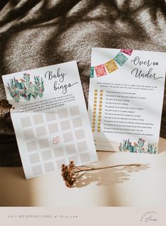 two baby shower games sitting on top of a bed next to a plant and paper