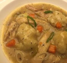 a white plate topped with chicken and dumplings covered in gravy next to carrots