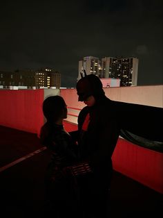 a man and woman standing next to each other in front of a city at night