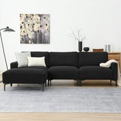 a black couch sitting on top of a wooden floor next to a lamp and table