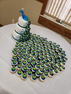 a cake and cupcakes on a table with a peacock decoration in the middle