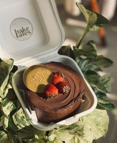 there is a cake with strawberries on top in a box next to some leaves