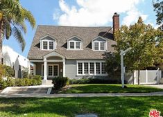 a gray house with white trim and two windows on the front, surrounded by palm trees