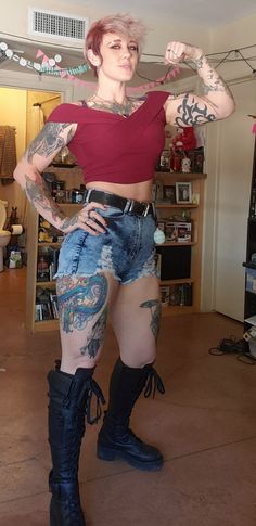 a woman in short shorts and boots with tattoos on her arms is posing for the camera