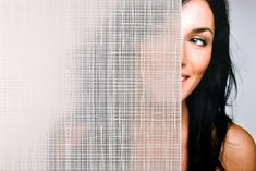 a woman with long black hair standing next to a white wall and looking at the camera