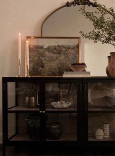 a glass cabinet with vases and candles on top in front of a wall mounted mirror