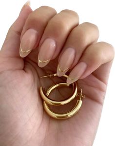 a woman's hand holding a pair of gold hoop earrings